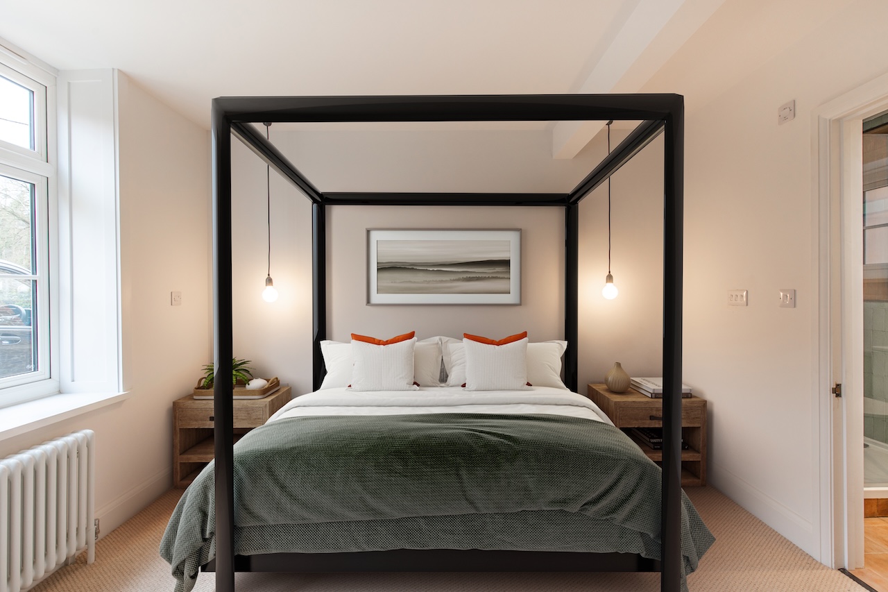 Master Bedroom Interior - Sophisticated master bedroom featuring black metal four-poster bed frame with sage green textured throw blanket, white striped bedding with orange accent pillows, wooden floating nightstands, pendant lighting, abstract landscape artwork, and en-suite bathroom visible through doorway creating an elegant sleeping space