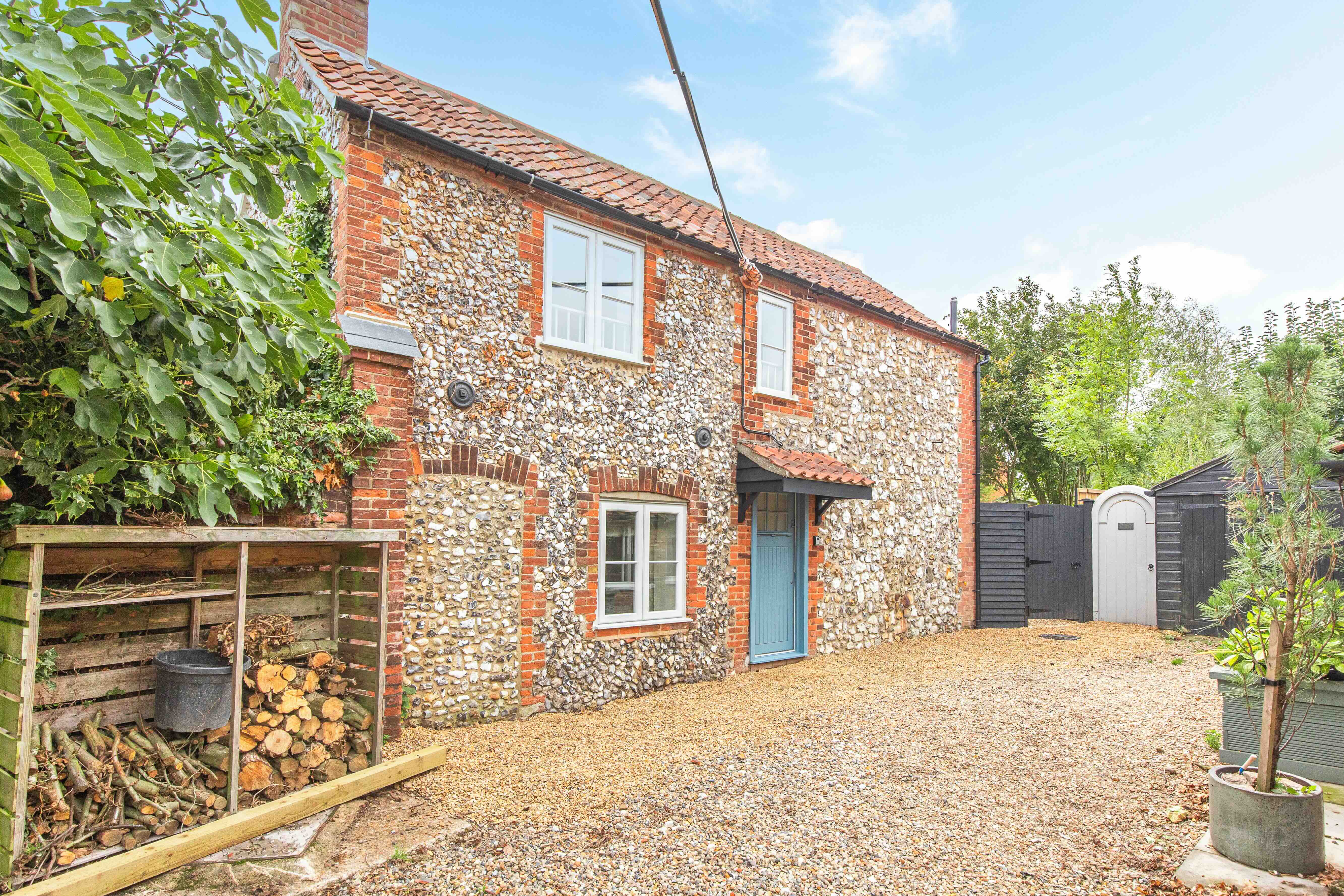 Flint Cottage exterior showing brick and flint walls, red tile roof, and blue front door